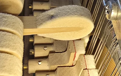 Hammer eines Klaviers schlägt gegen die Saiten, während der Dämpfer von den Saiten abgehoben ist.